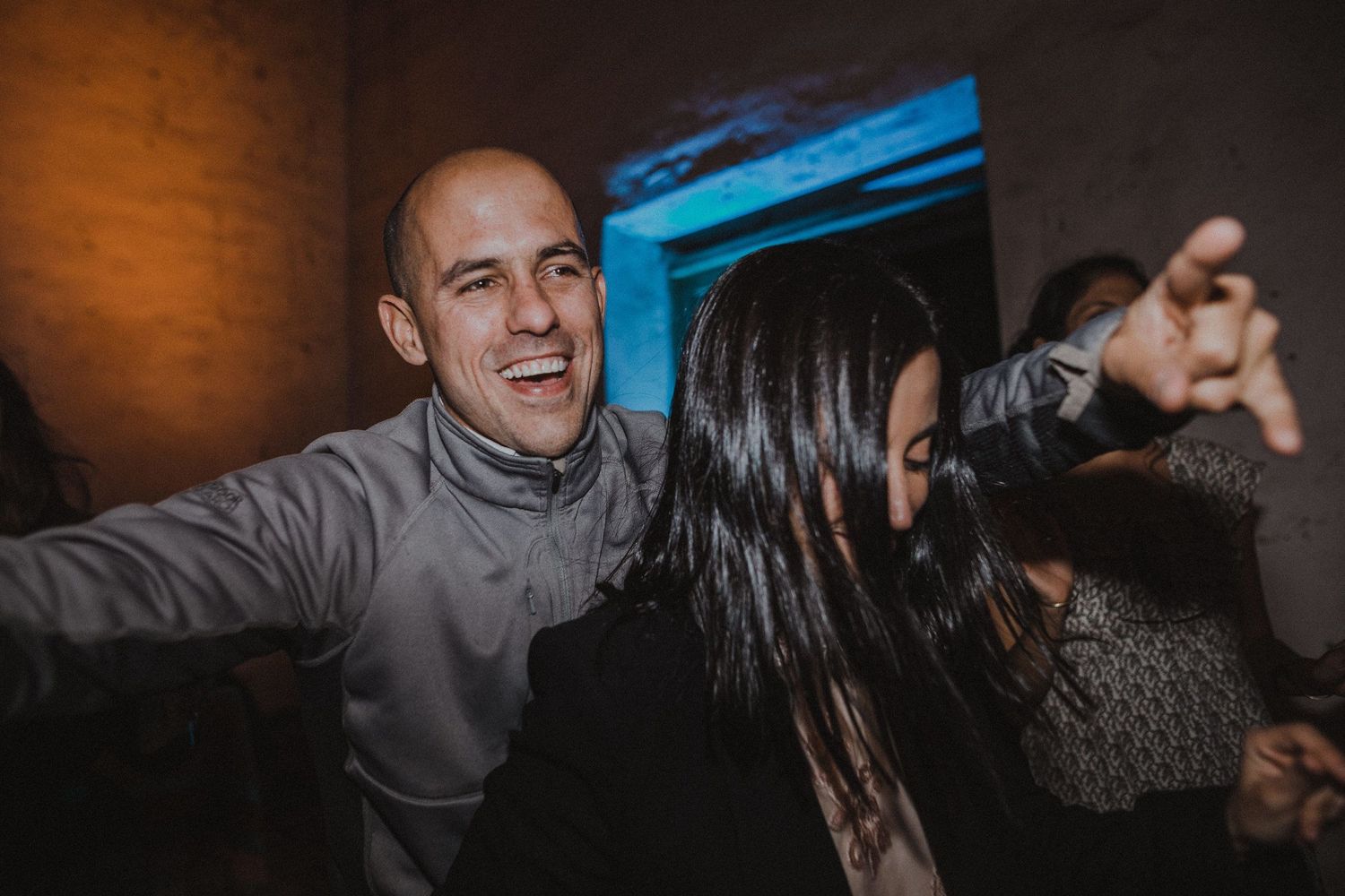 Dancing guests enjoying lively celebration at dimly lit indoor venue.