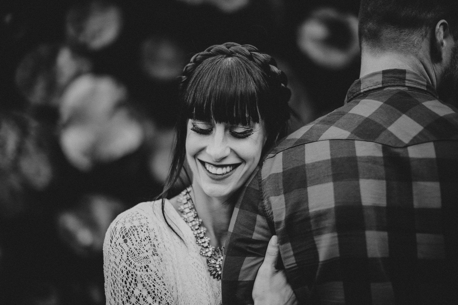 Black and white portrait of person in lace dress smiling with plaid shirt in background.