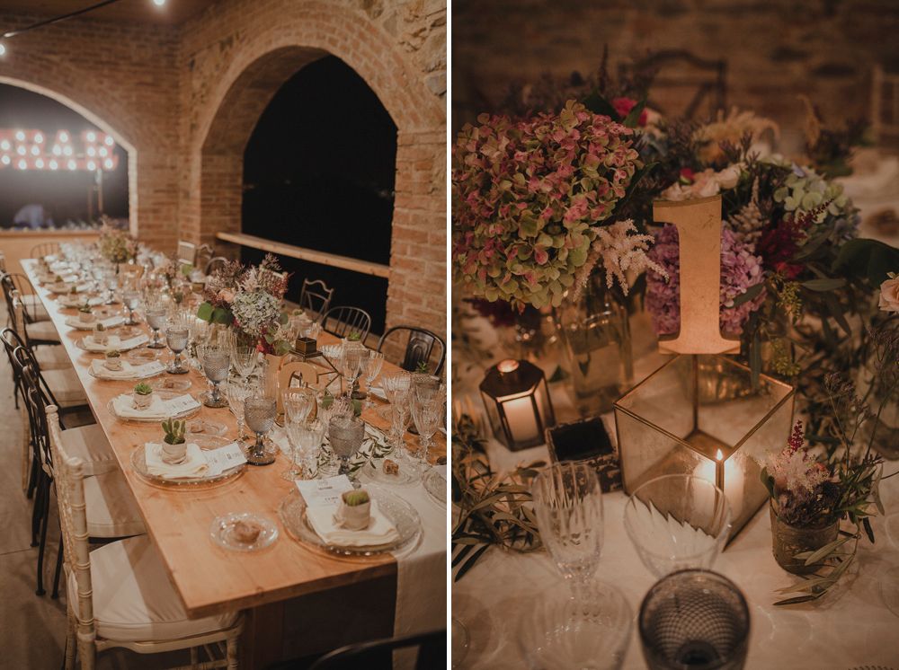Rustic wedding reception table setup with lanterns and floral arrangements in stone archway.