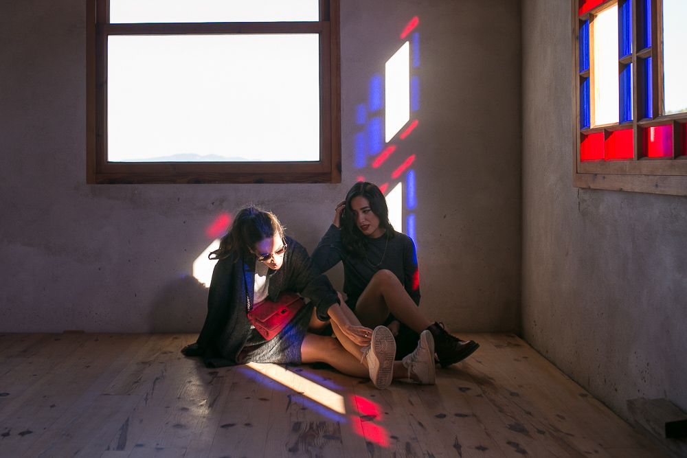 Two people sit on a wooden floor with colorful light streaming through windows.