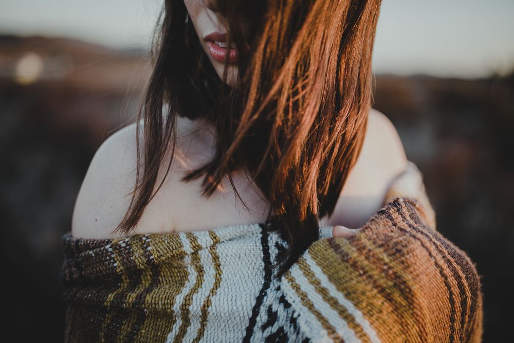 An artistic portrait showing someone wearing an off-shoulder patterned sweater at sunset.