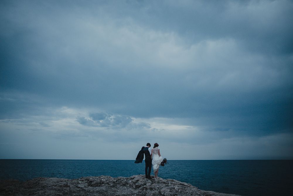 Two figures stand together on a dramatic oceanside cliff during golden hour.