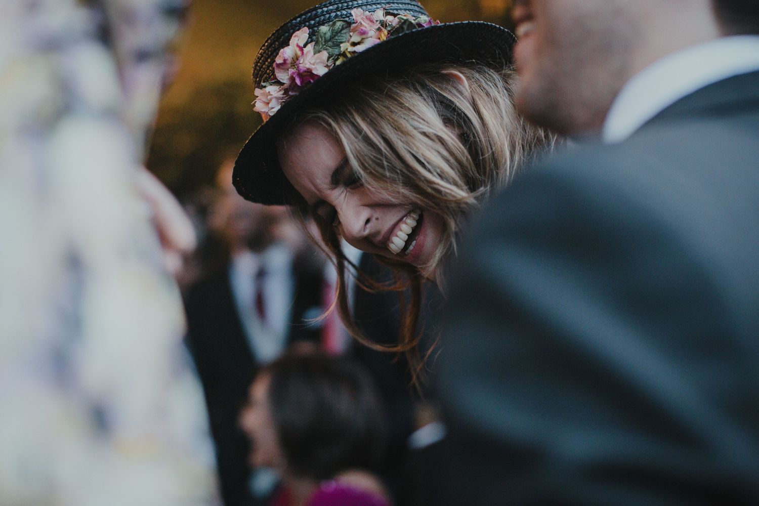 Wedding guest wearing a floral crown laughs during an outdoor celebration.