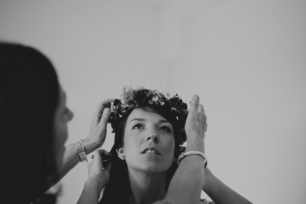 Black and white image of a delicate flower crown being placed during wedding preparations.