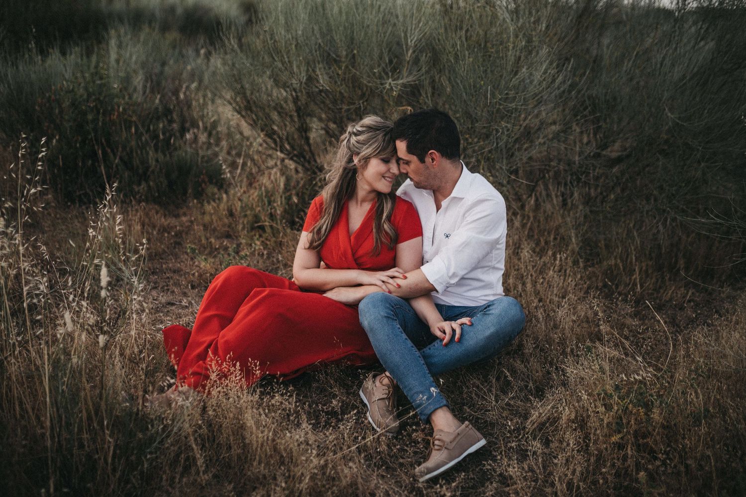Couple sitting in dry grass field sharing romantic moment outdoors.