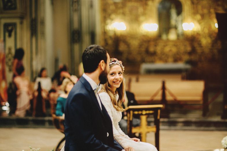 A couple shares an intimate moment during their wedding ceremony in an ornate church with glowing chandeliers.
