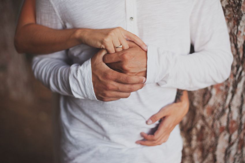 Close-up of hands holding and intertwining against white clothing.