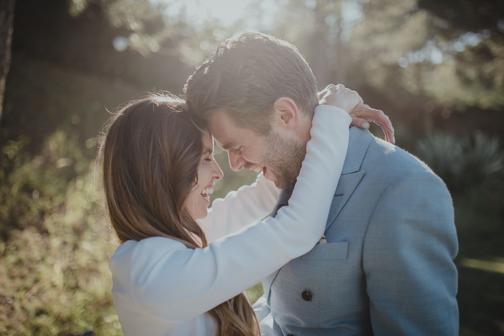 Tender moment captured between couple in light blue suit and white dress outdoors.