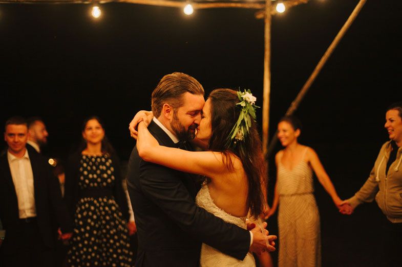 Newlyweds share their first dance under string lights as guests watch from the sidelines.