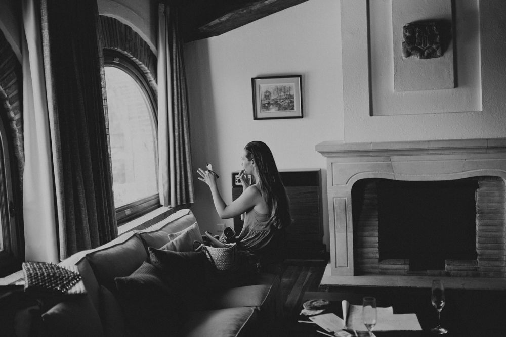 A person relaxes by a window while reading in a cozy room with a fireplace.