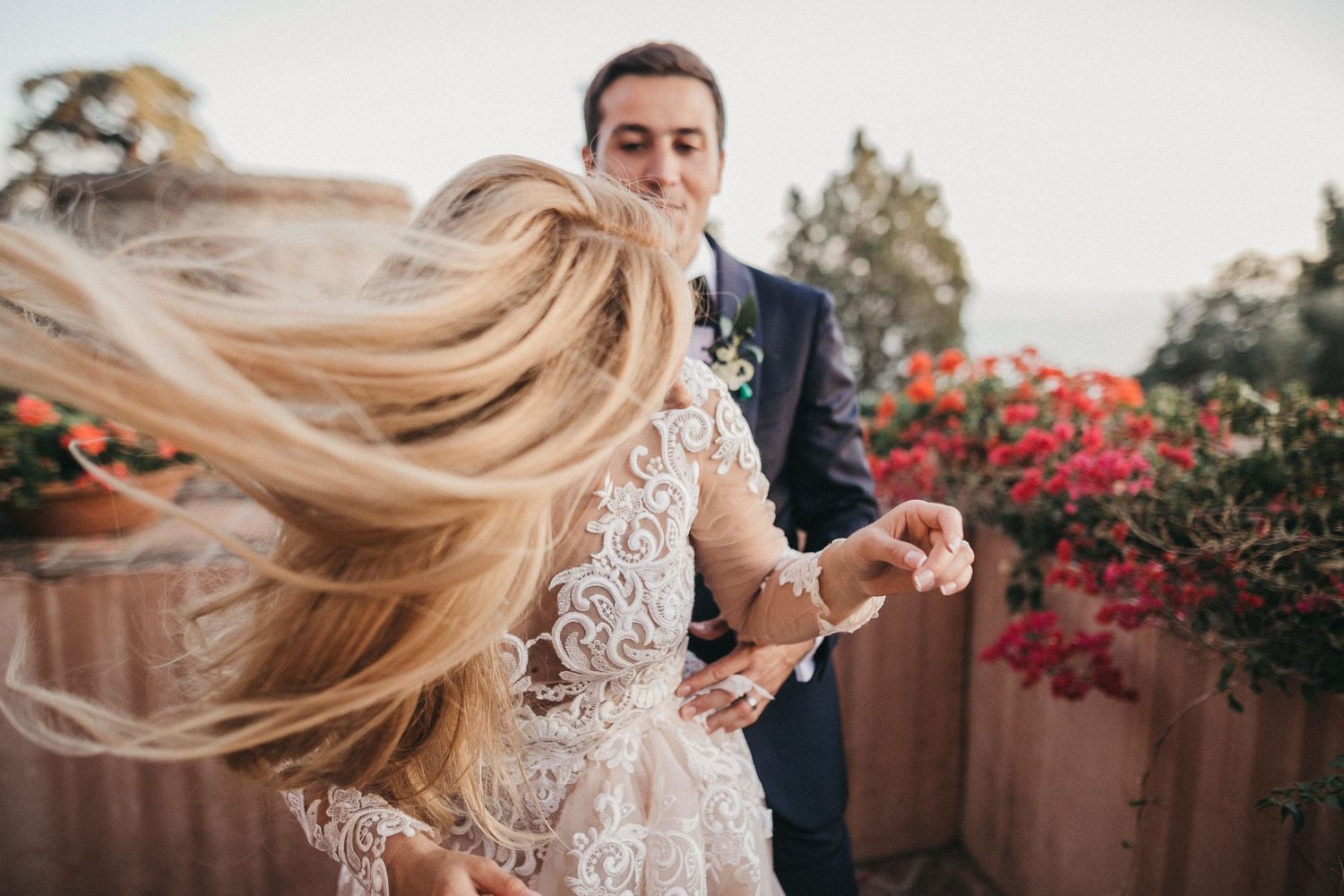 Bride's long hair flows in the wind while dancing with groom among red flowers.