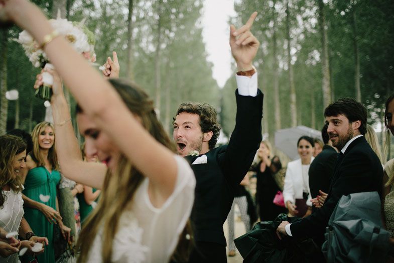 Wedding guests celebrate joyfully with raised arms at an outdoor forest reception.