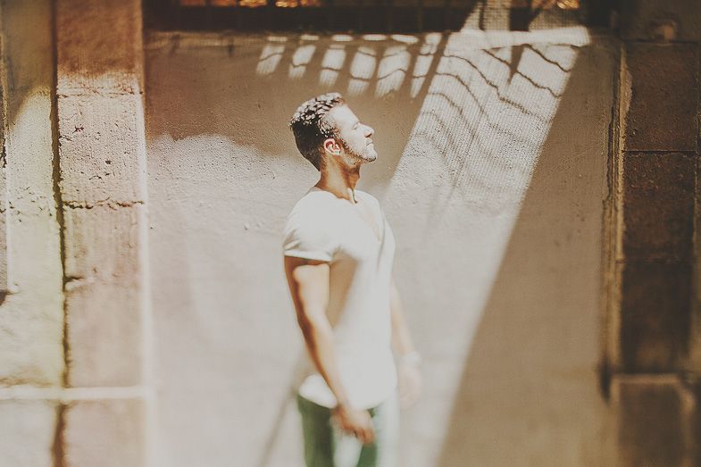 A person in white stands in dramatic sunlight streaming through an architectural space.