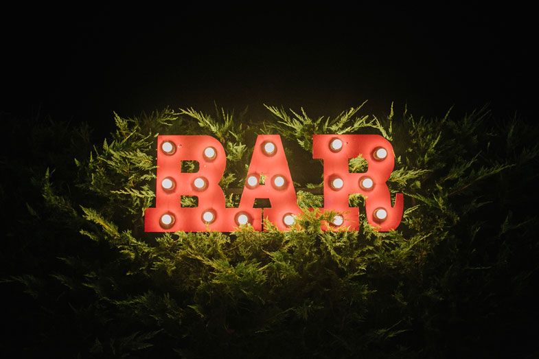 Illuminated BAR sign with red marquee lights displayed in grass at night.