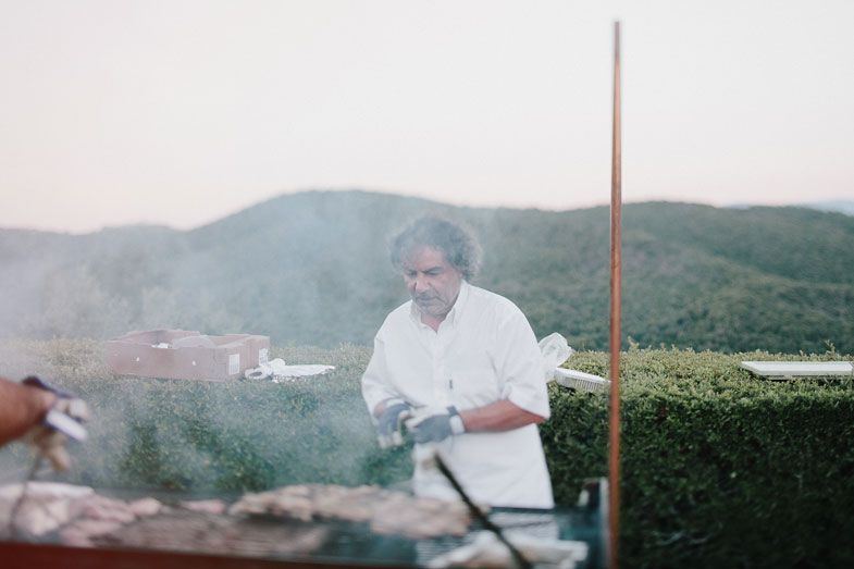 Chef preparing food at an outdoor barbecue station with hills in background.
