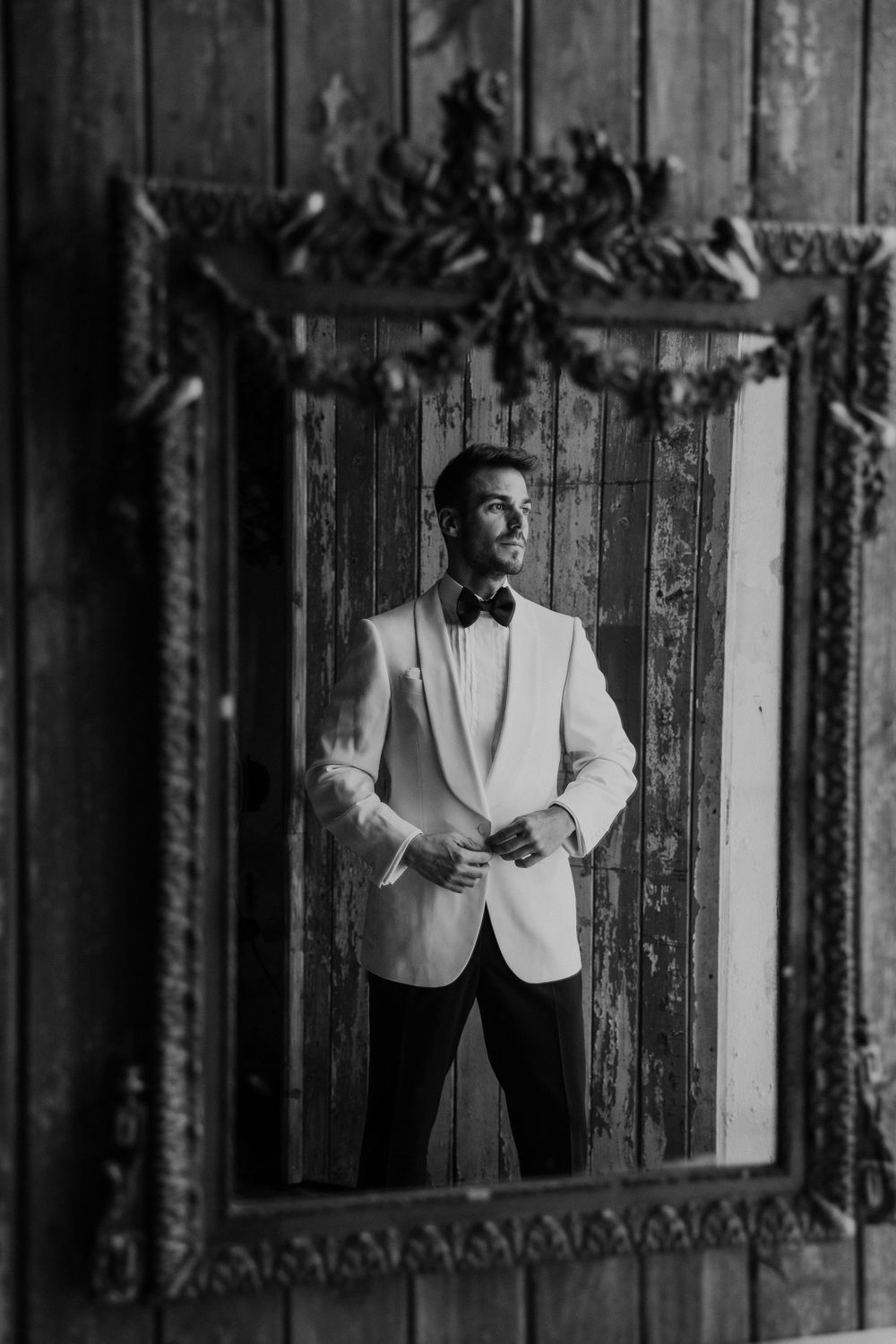 Black and white portraits of groom in white tuxedo jacket against vintage wooden panels.