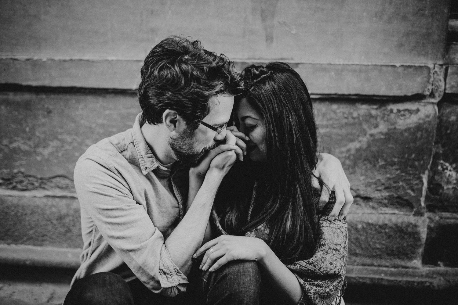 Black and white portrait showing tender moment between couple against stone wall.