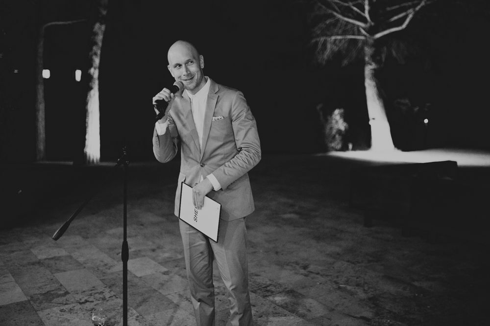 A person in a light suit delivers a speech outdoors at night.
