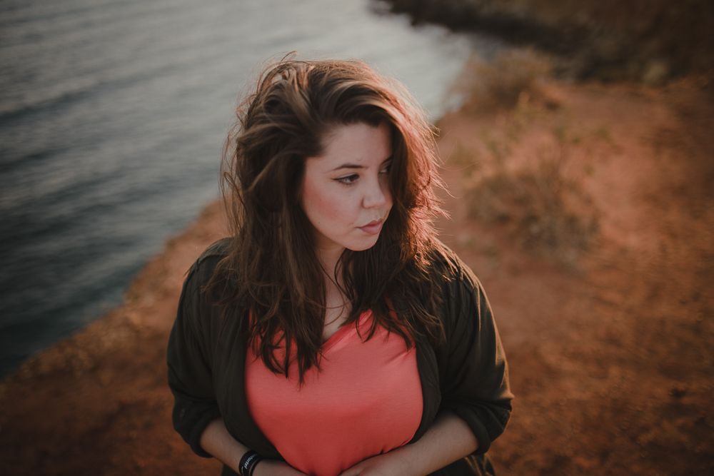 Portrait of woman in coral top and black jacket looking away during sunset.