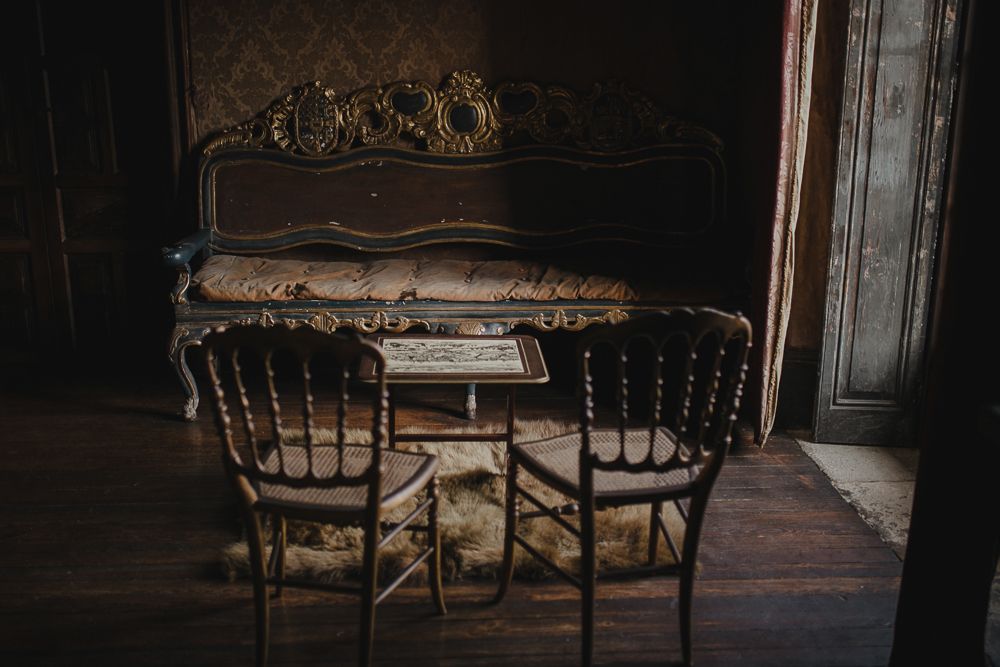 Vintage antique piano and wooden chairs in a dimly lit room with dark wood floors and ornate details.