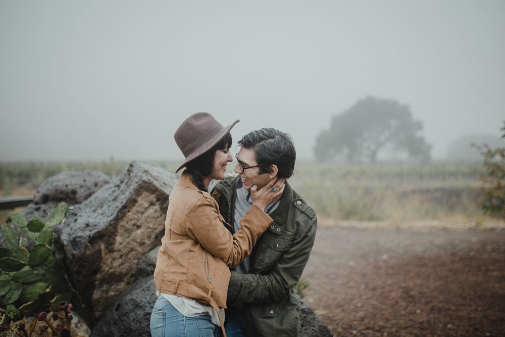 A misty outdoor scene with two figures by large rocks in nature.