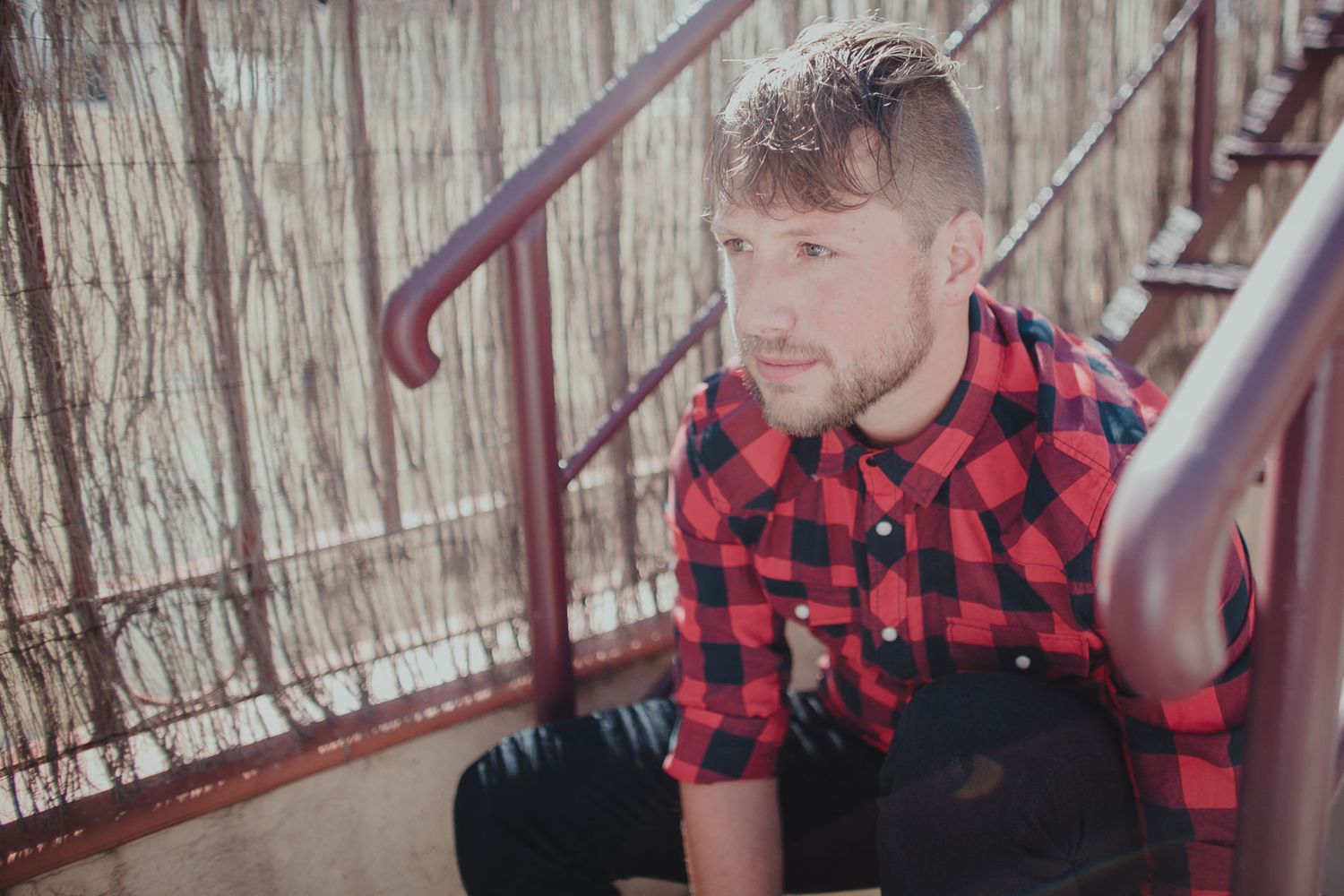 Person in red buffalo plaid shirt sitting on outdoor metal stairs.