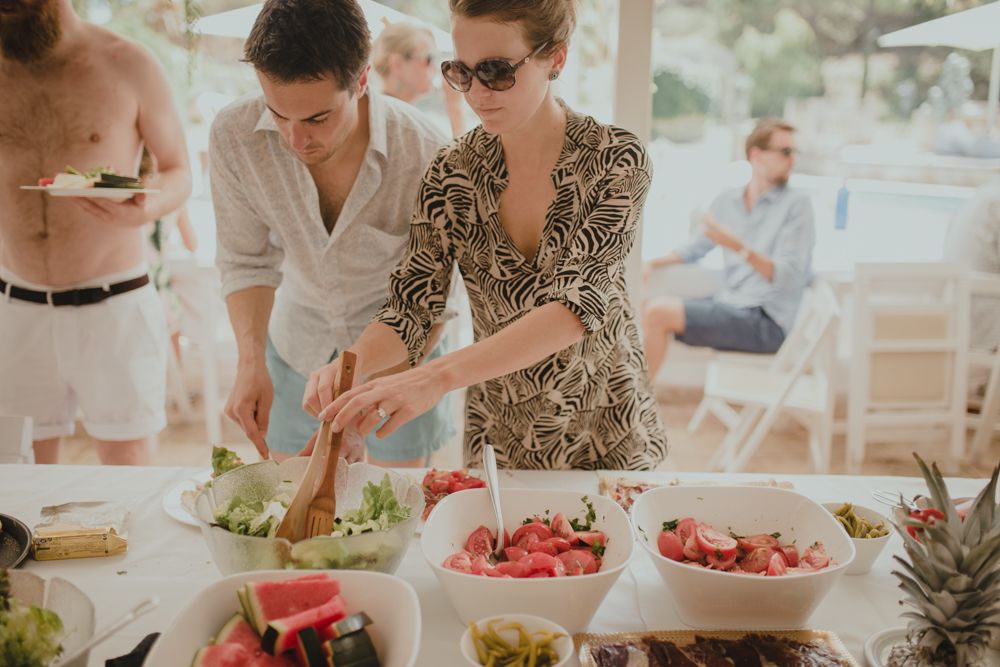Party guests serving themselves from a buffet spread with fresh fruits and salads.