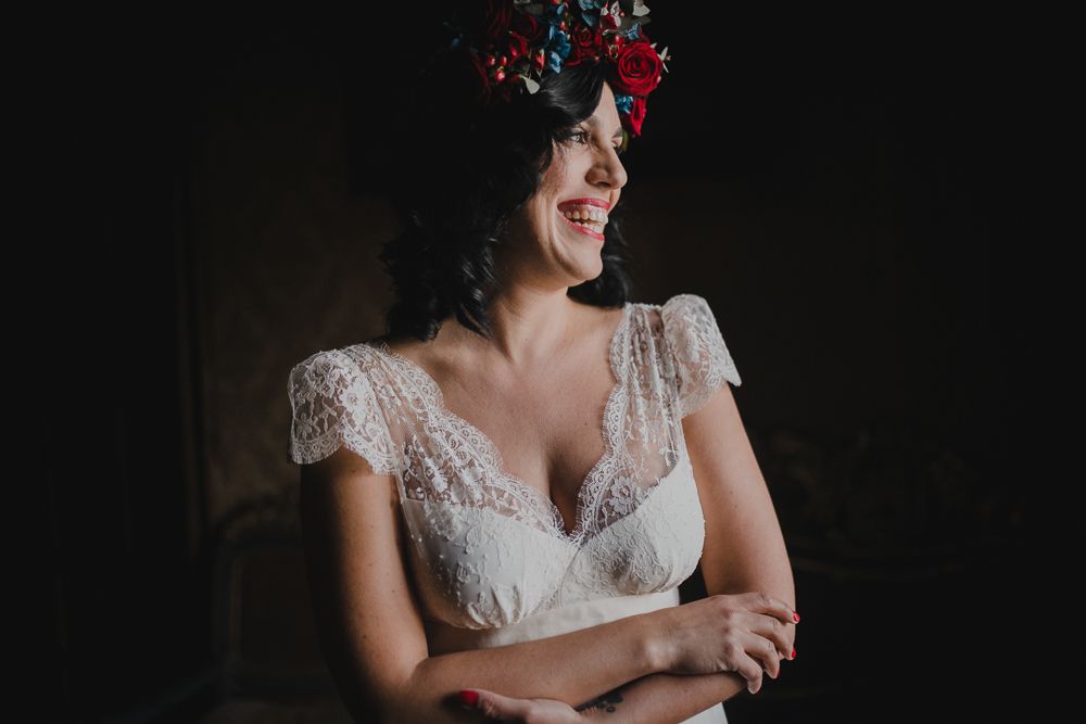 A joyful bridal portrait featuring a lace dress and red floral crown in dramatic lighting.