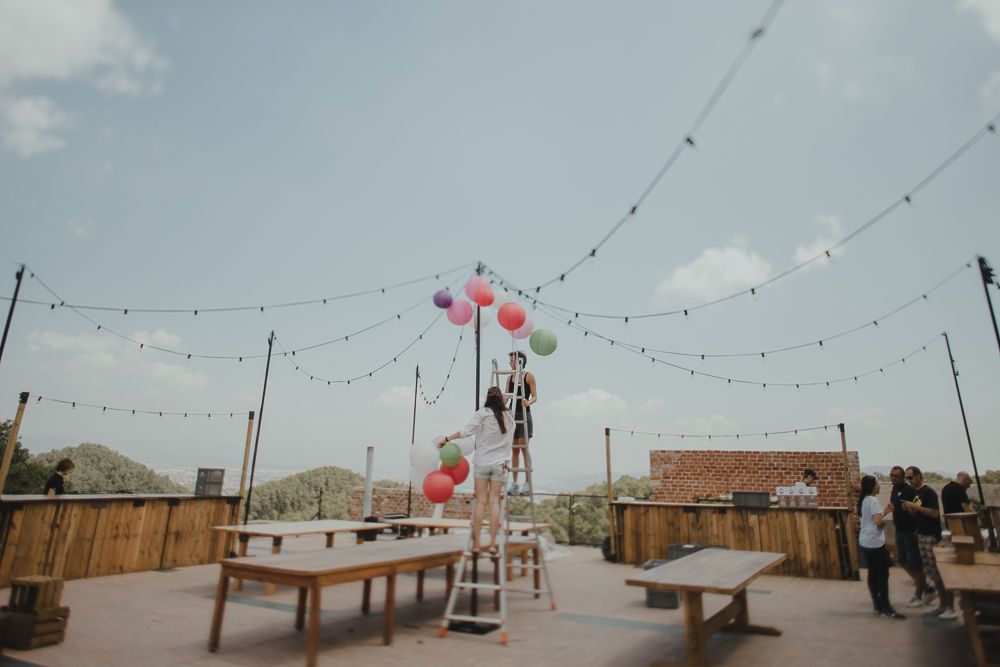 Outdoor rooftop venue with string lights and red balloons being set up for an event.