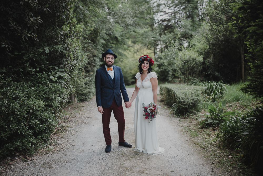 A couple standing on a forest path in wedding attire holding hands.