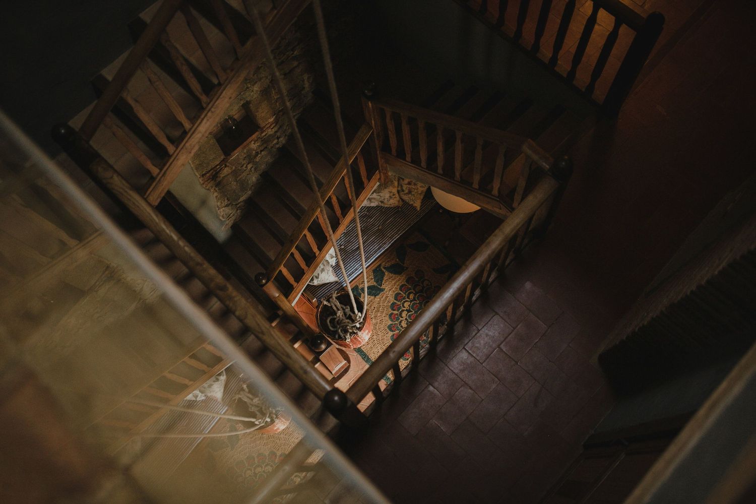 Dramatic overhead view looking down a dimly lit spiral staircase with wooden railings.