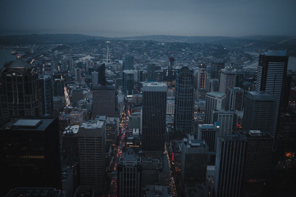 Aerial view of a dark cityscape with tall skyscrapers and illuminated streets at dusk.
