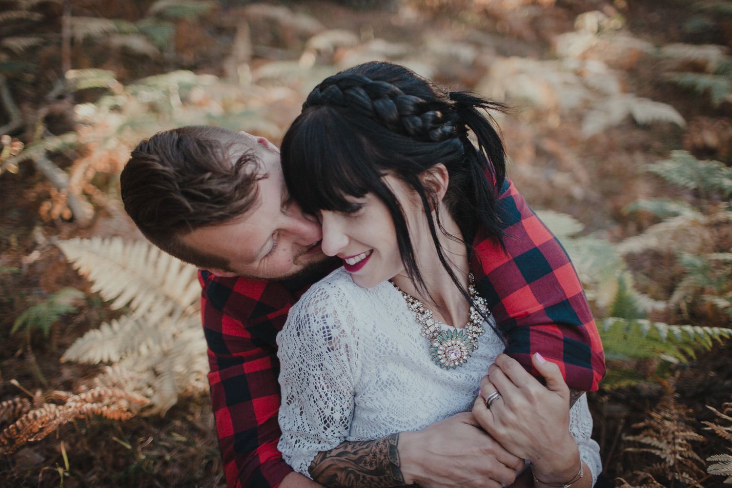 A romantic embrace among autumn ferns with plaid and lace attire creating a cozy woodland scene.