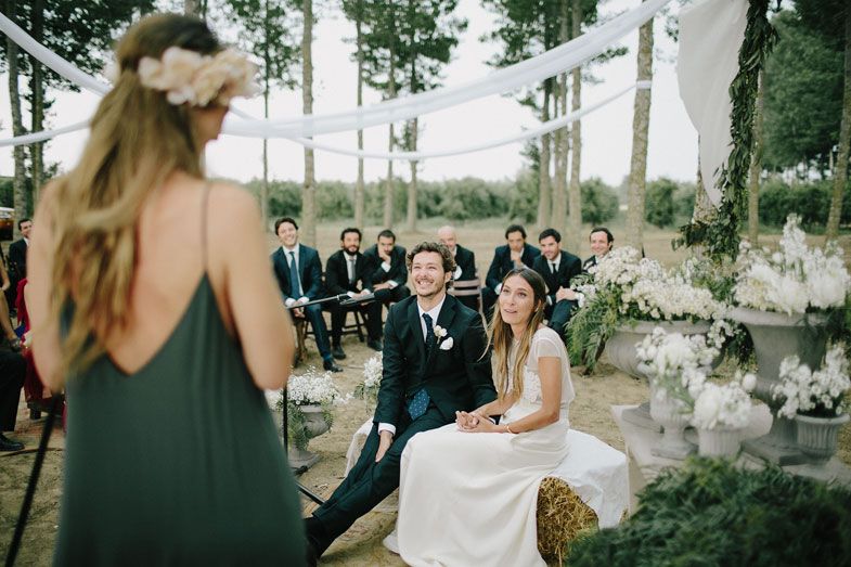 Outdoor woodland wedding ceremony with white drapes and floral arrangements among aspen trees.