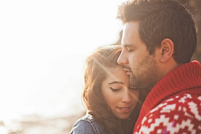 Intimate portrait of a couple in winter attire embracing in warm sunlight.