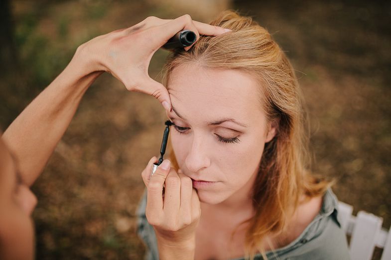 Detailed makeup application being performed with careful precision outdoors.