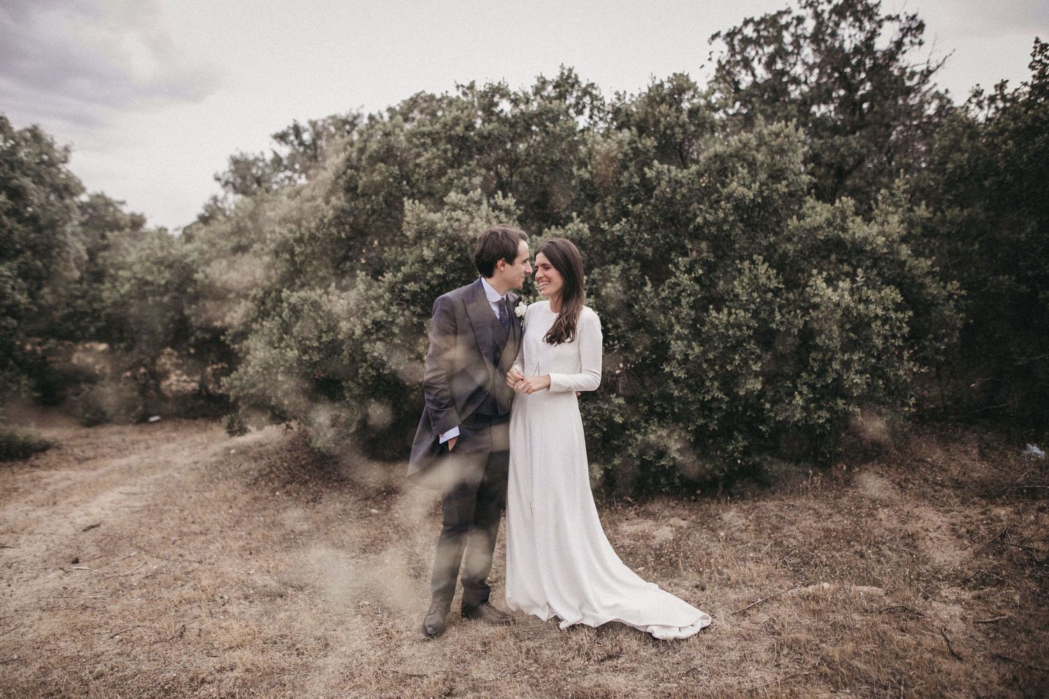 A dreamy wedding portrait in a rustic outdoor setting with natural vegetation.
