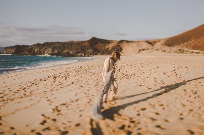Person walking alone on a sandy beach with coastal cliffs in the background.