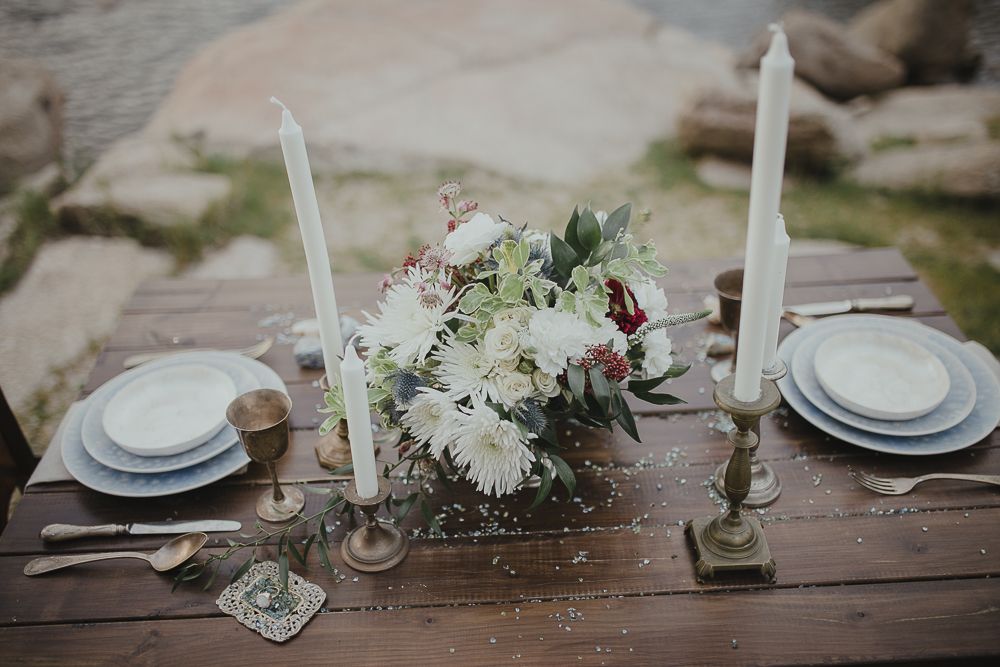 Rustic table decorated with white flowers, candles and place settings by the water.