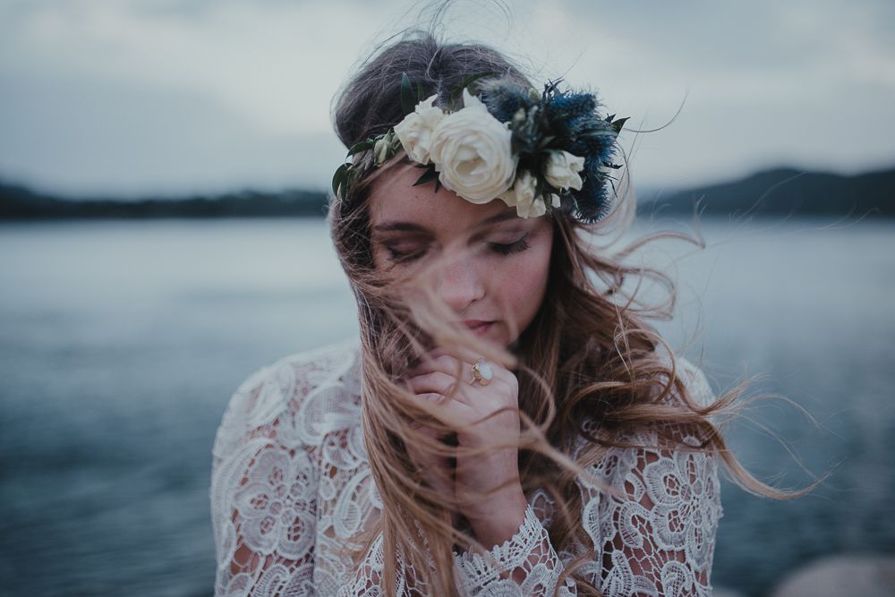 Ethereal bridal portrait with white flower crown against misty lake landscape.