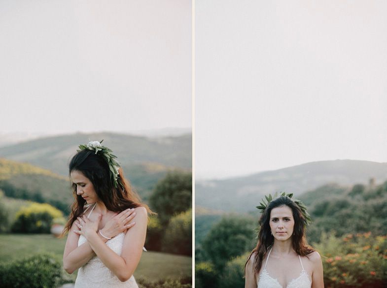 Bride wearing lace dress and flower crown stands in mountain field during sunset.