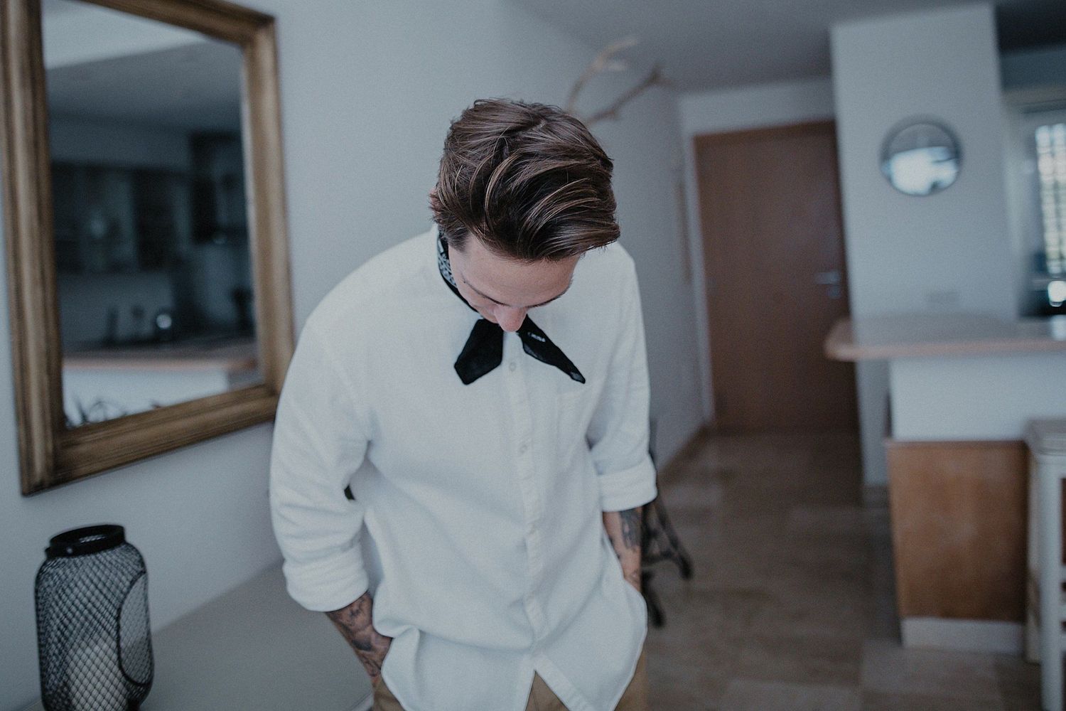 A person in formal white attire adjusting their bowtie while looking down.
