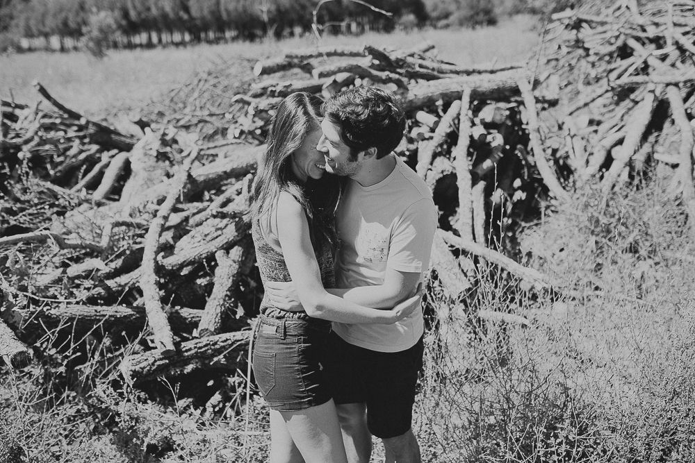 Couple embracing near rustic woodpile in black and white photography.