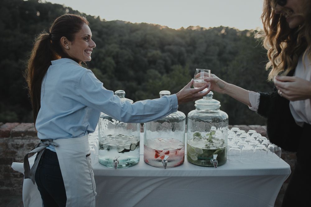 Server pouring drinks at an outdoor event bar with glass jars of cocktails.