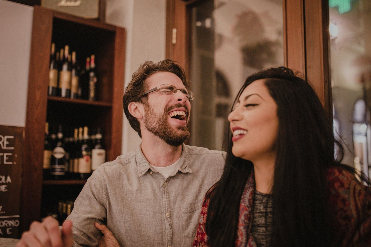 A couple shares a genuine laugh together in a warmly lit restaurant setting.