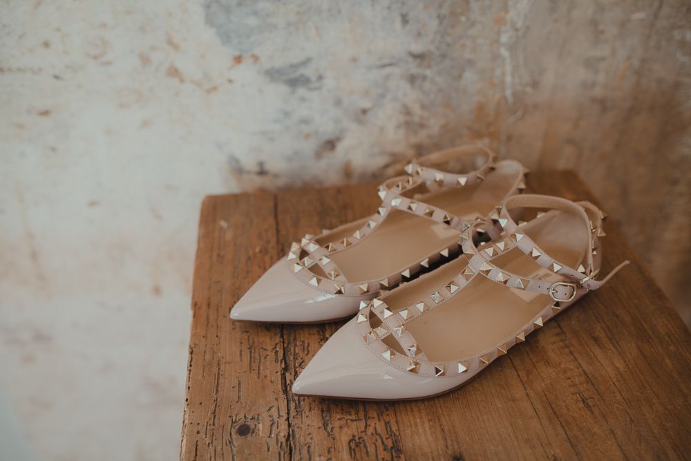 Studded nude flats with pointed toes sit on a wooden surface.