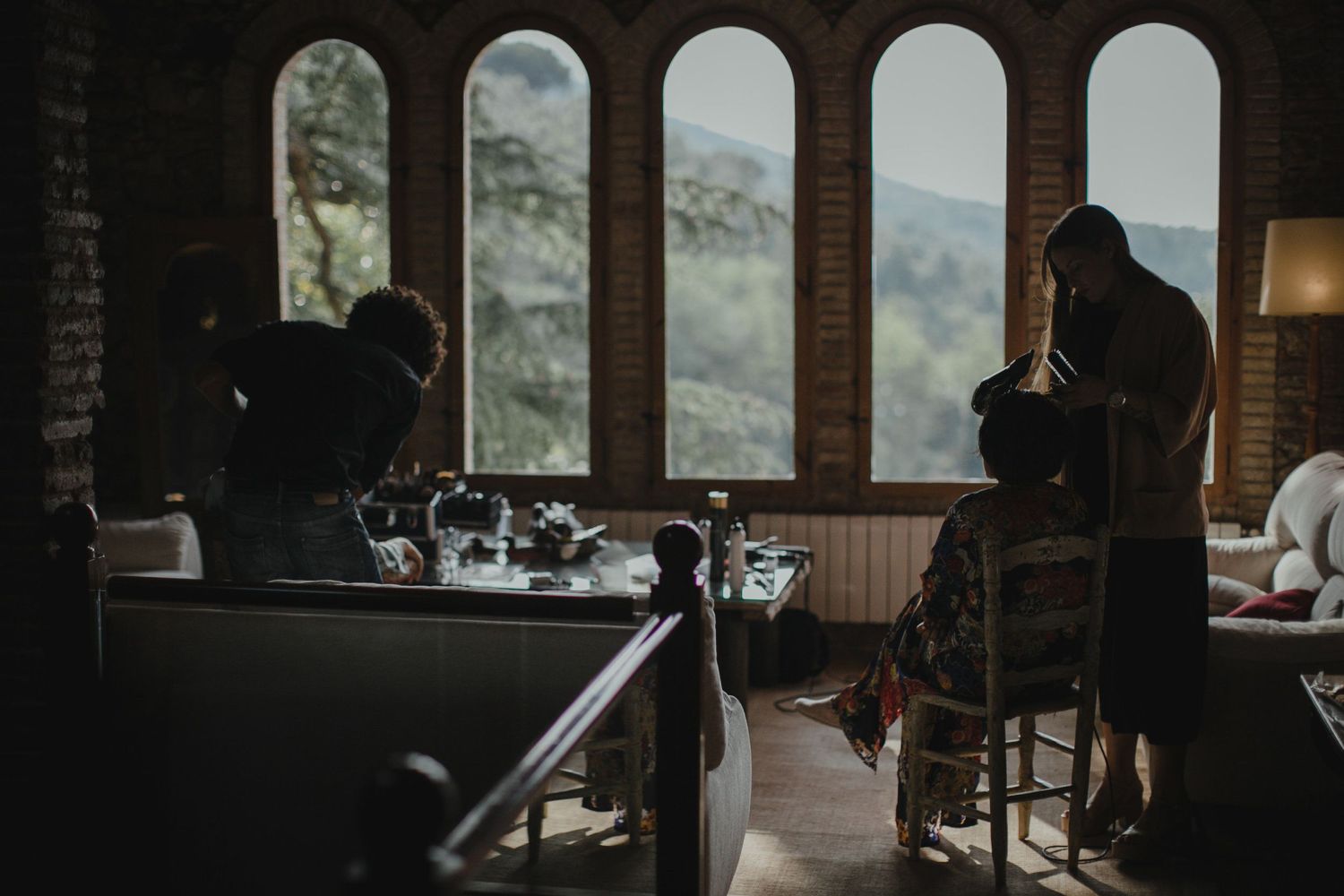 Silhouettes in a room with arched windows overlooking a scenic mountain landscape.