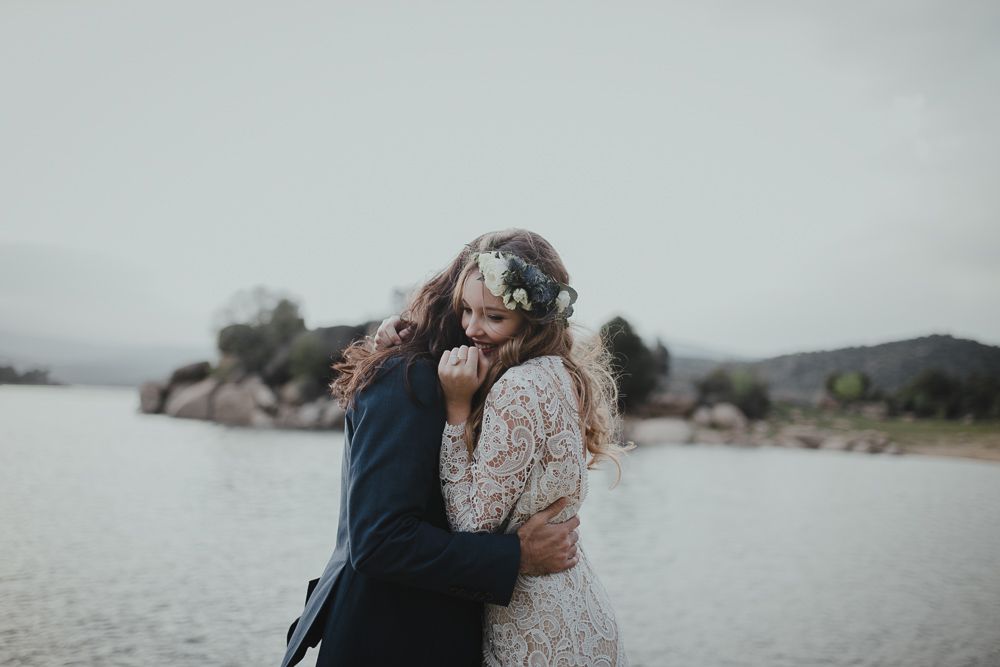 A romantic moment captured between a couple embracing by a misty lake with rocky outcrops in the background.