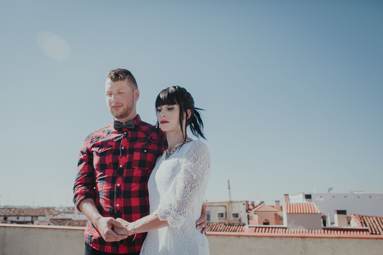 Stylish couple in red plaid and white lace pose together on urban rooftop with cityscape backdrop.