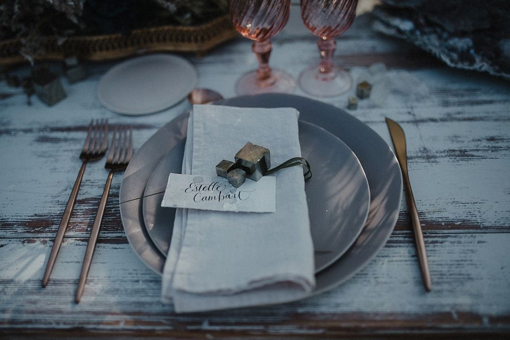 Elegant place setting with pink glasses, silver utensils and a menu card on a rustic wooden table.